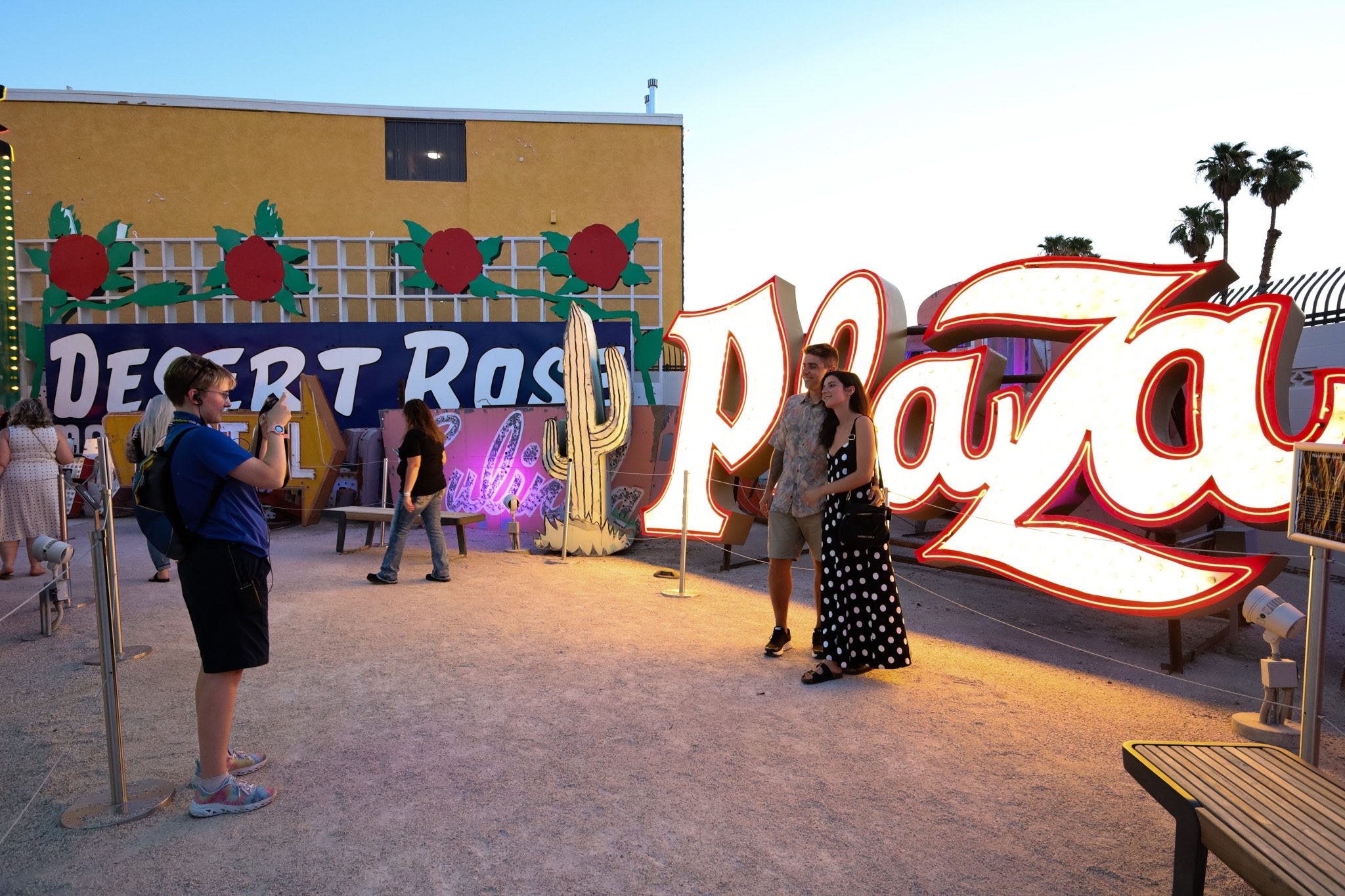 A museum guide takes the picture of a couple in front of the Plaza sign at The Neon Museum's Neon Boneyard.
