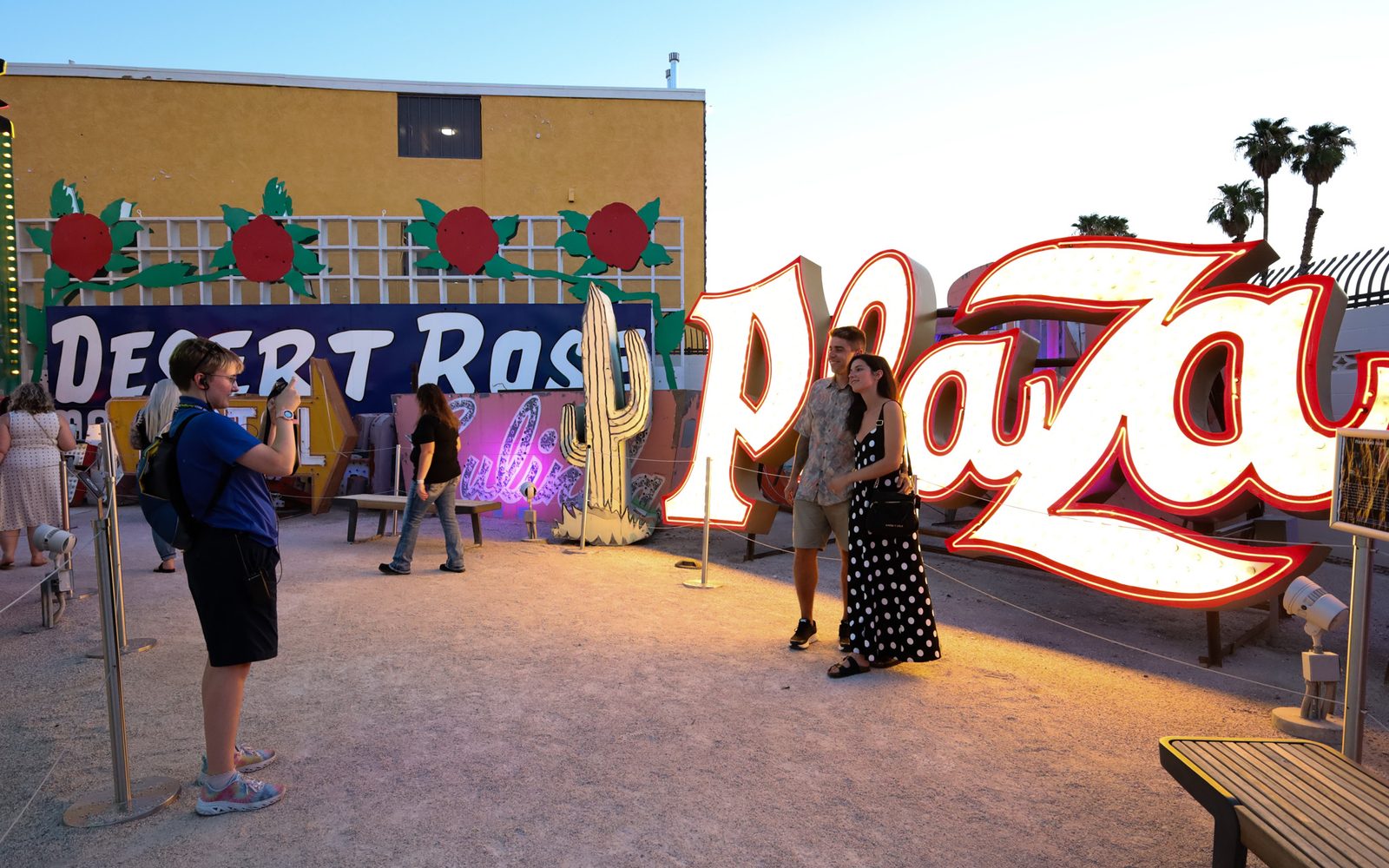 A museum guide takes the picture of a couple in front of the Plaza sign at The Neon Museum's Neon Boneyard.