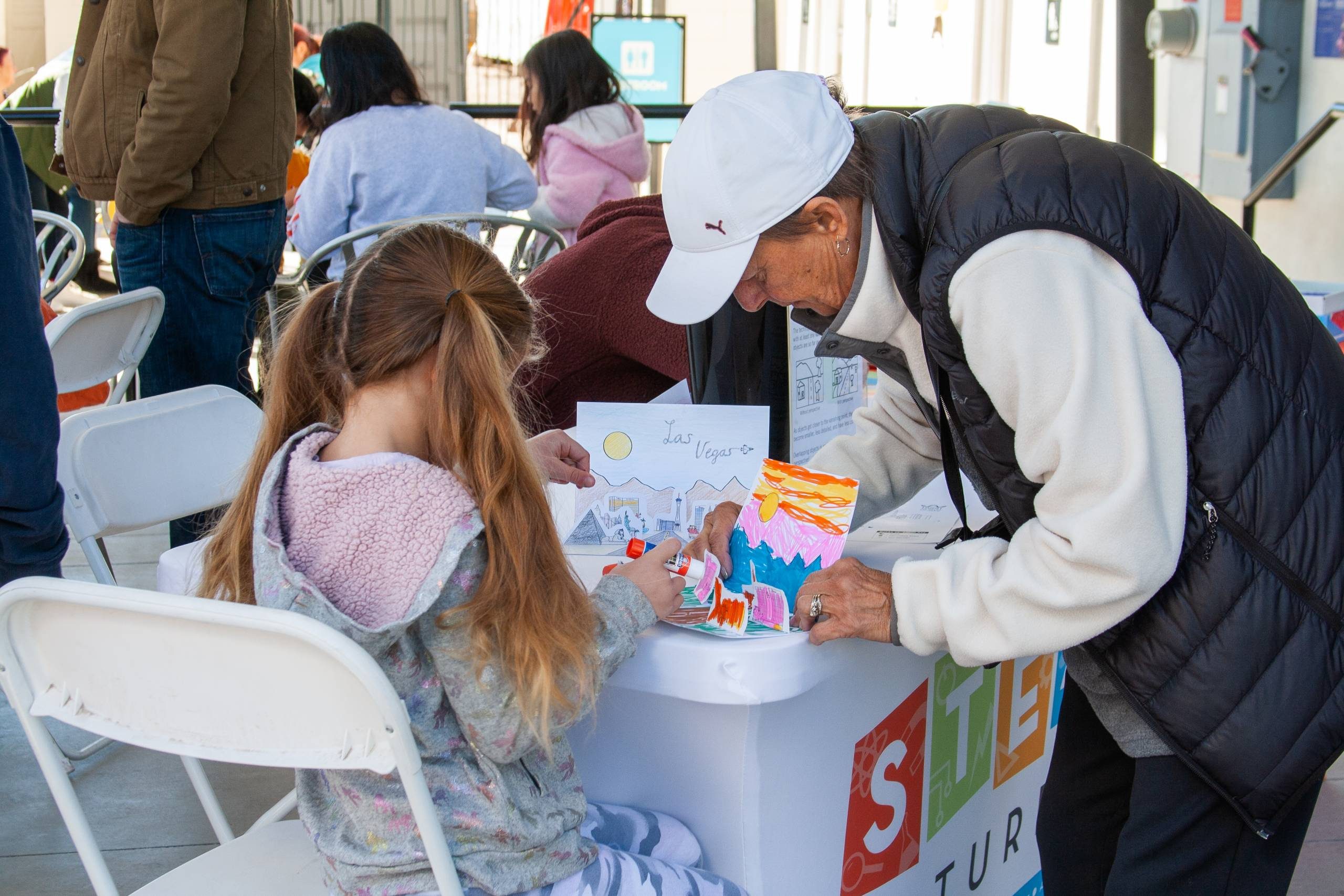 A parent helps their child glue on their project during a STEAM Saturday event at The Neon Museum.