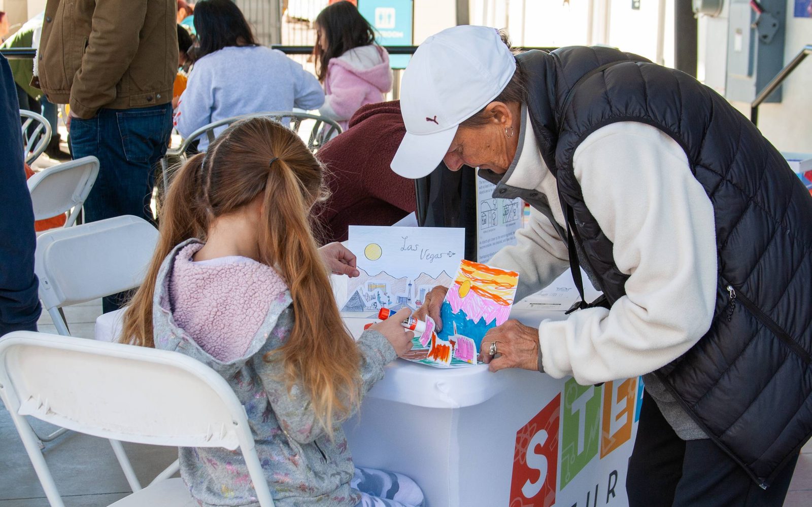 A parent helps their child glue on their project during a STEAM Saturday event at The Neon Museum.