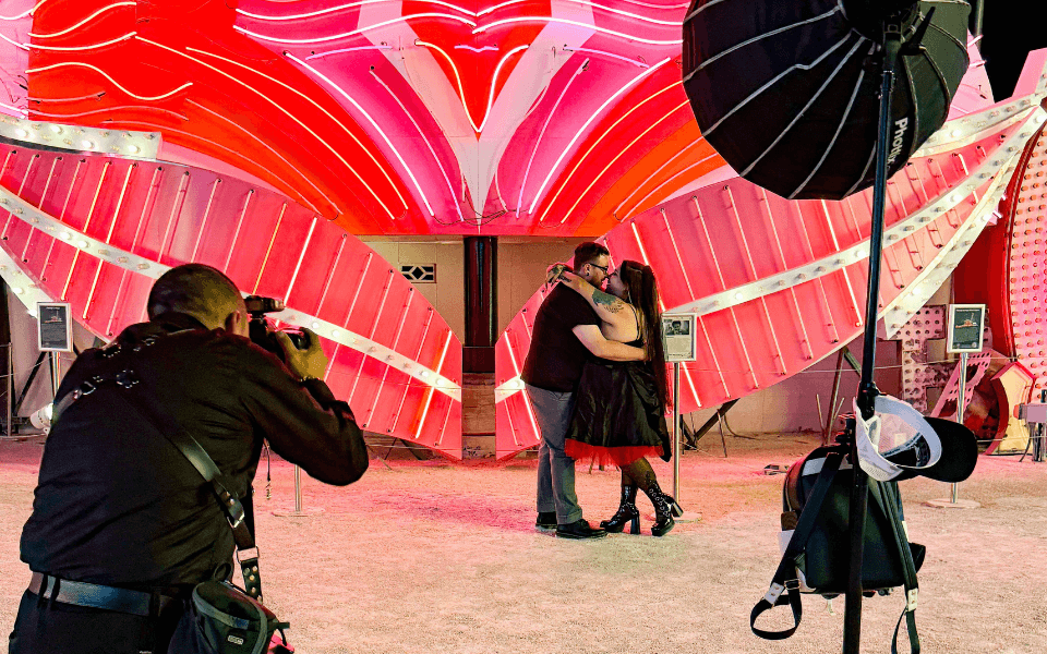 A photographer with their equipment taking a picture of a couple in front of the Flamingo sign.