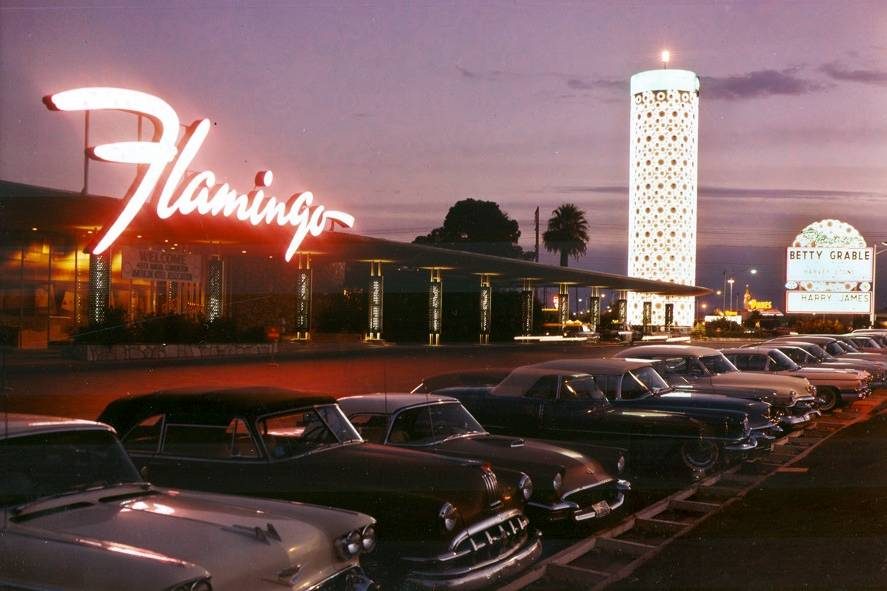 Exterior view of the Flamingo Hotel at sunset, the illuminated champagne tower and a marquee are visible, UNLV Special Collections, mid 1950s
